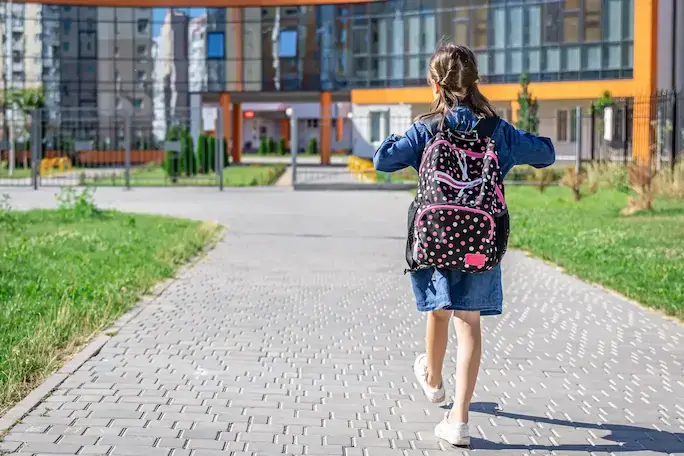 Young girl with a backpack walking along a path to school